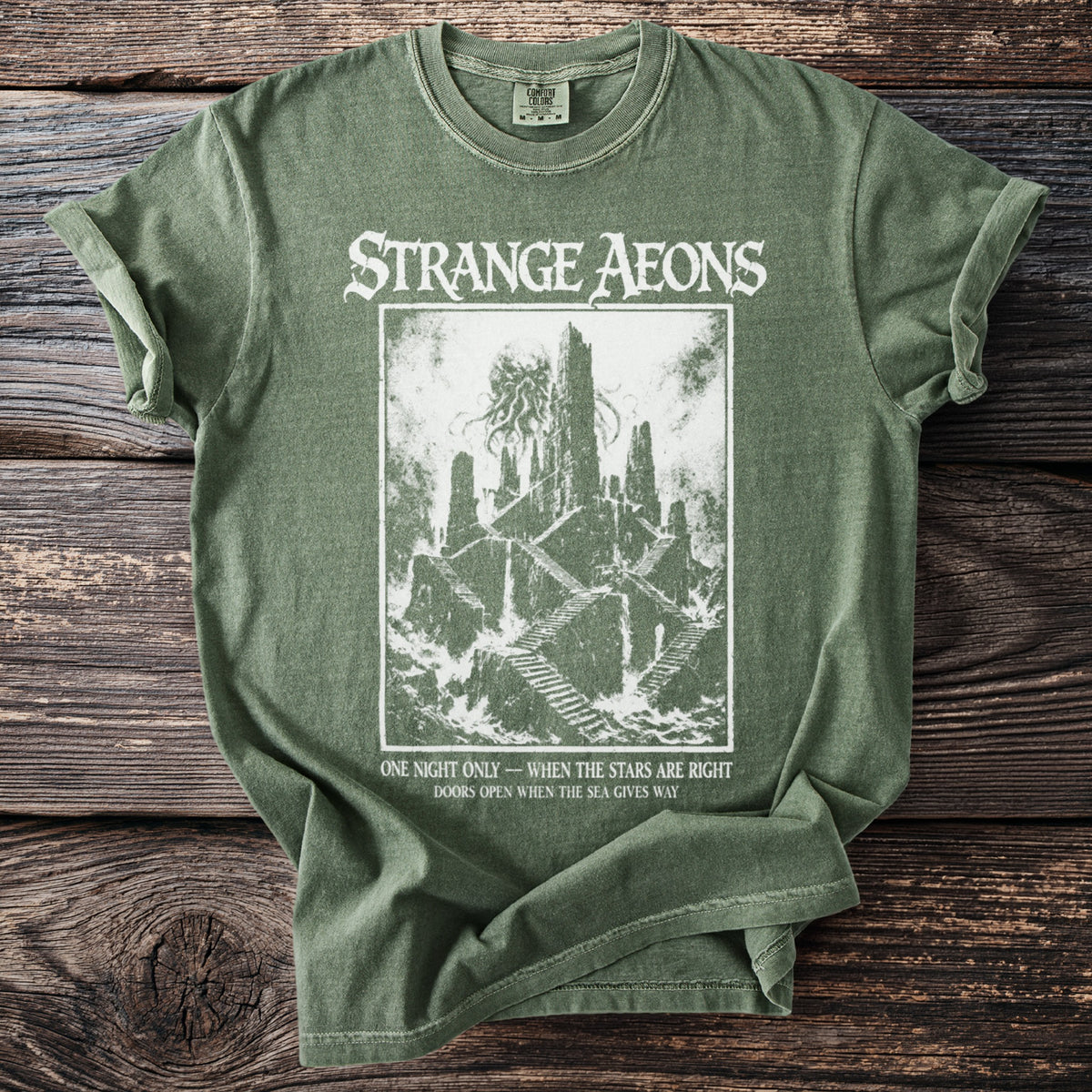 Green t-shirt with "STRANGE AEONS" and a dark fantasy castle illustration.