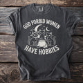 T-shirt with white graphic of three cats, cauldron, skeleton and moon, reading "God Forbid Women Have Hobbies".