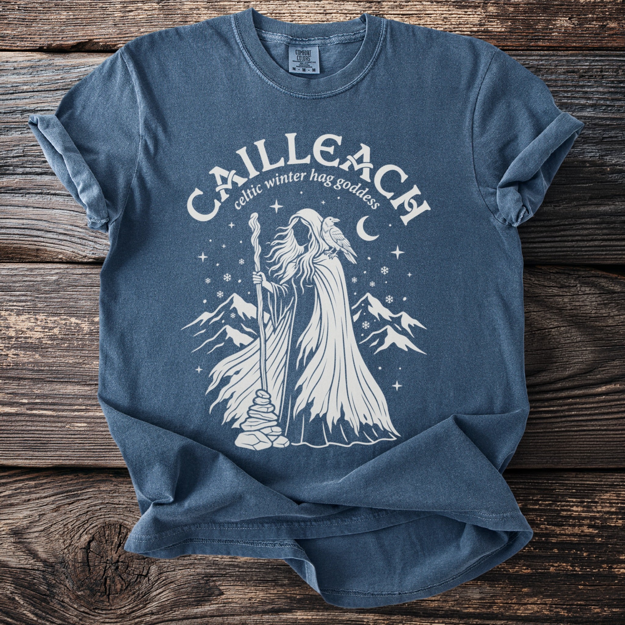 Celtic Cailleach winter hag goddess with crow and mountains on blue t-shirt.