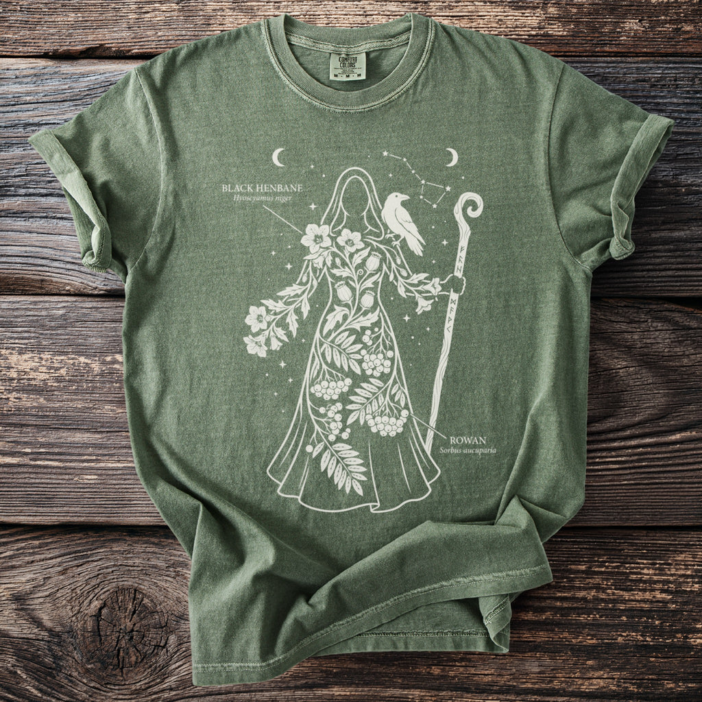 Green t-shirt with white outline of a figure adorned with plants, raven, and staff.