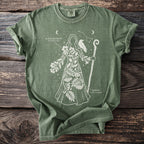 Green t-shirt with white outline of a figure adorned with plants, raven, and staff.
