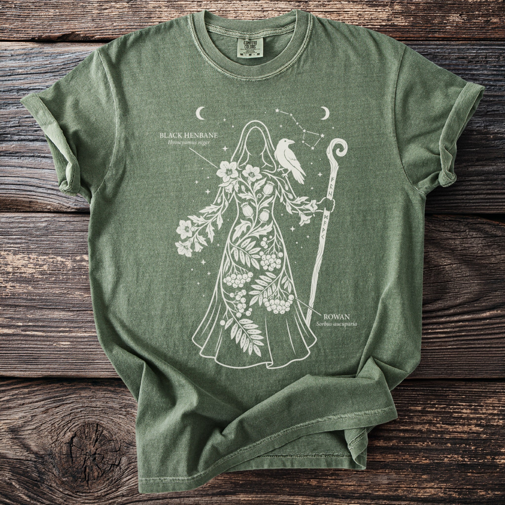 Green t-shirt with white outline of a figure adorned with plants, raven, and staff.