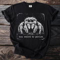 Black t-shirt with a vintage graphic of a jumping spider and the text "too weird to perish".
