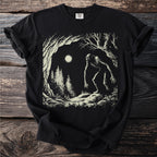 Black t-shirt with a Bigfoot in a forest illustration under moonlight.