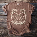 Brown t-shirt with cream graphic of a mothman-like creature and trees.