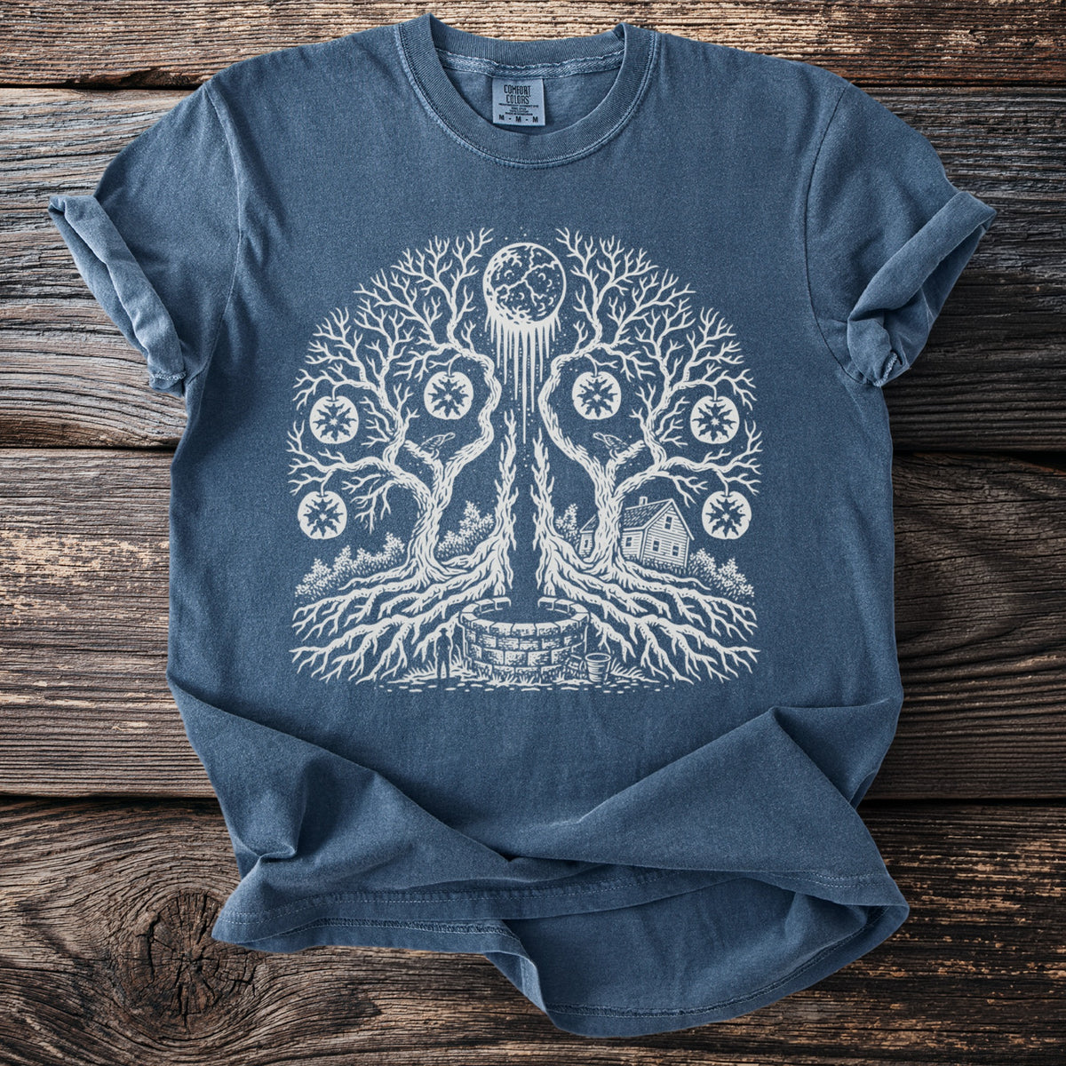 Blue t-shirt with white graphic of a tree, moon, well, house, and suns.