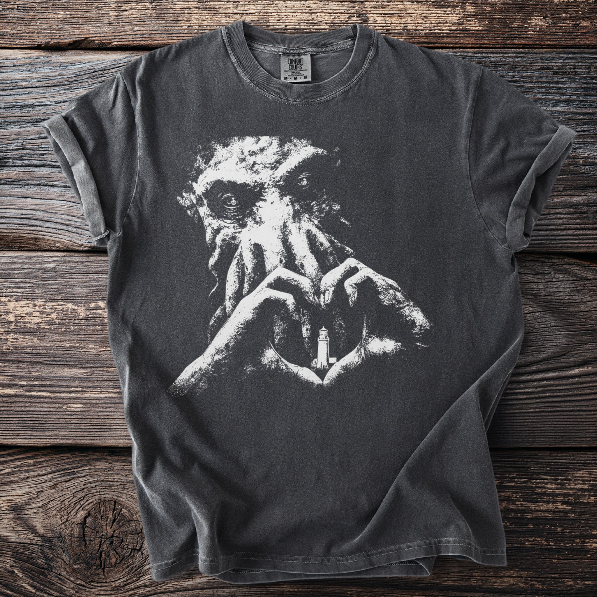 Dark t-shirt with white graphic of Cthulhu's face and hands forming heart around a lighthouse.