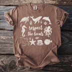 Brown t-shirt with a white graphic of marine animals and text that says "respect the locals."