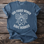 Blue t-shirt with white text: "God Forbid Women Have Hobbies" and graphics.