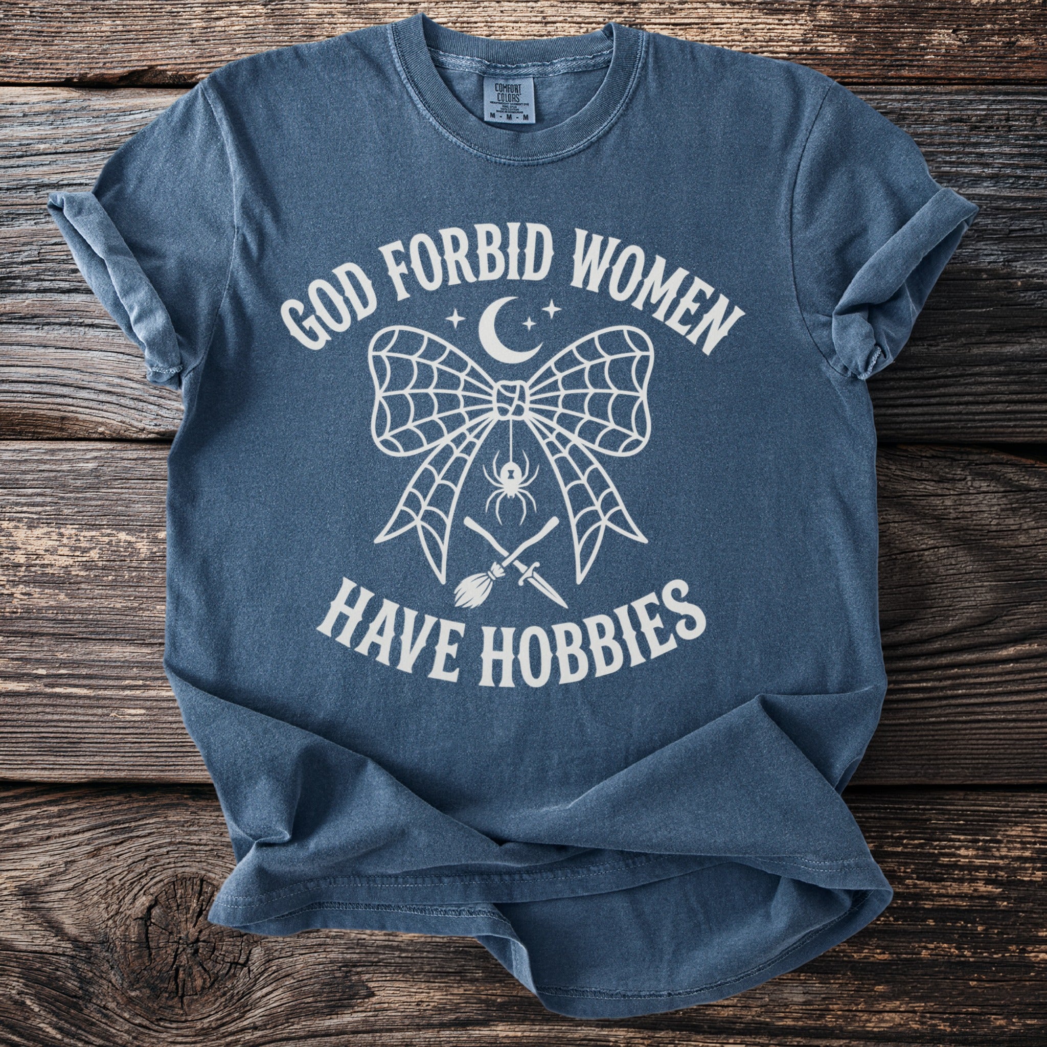 Blue t-shirt with white text: "God Forbid Women Have Hobbies" and graphics.