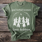 Green t-shirt with witches holding hands and text "god forbid women have hobbies".