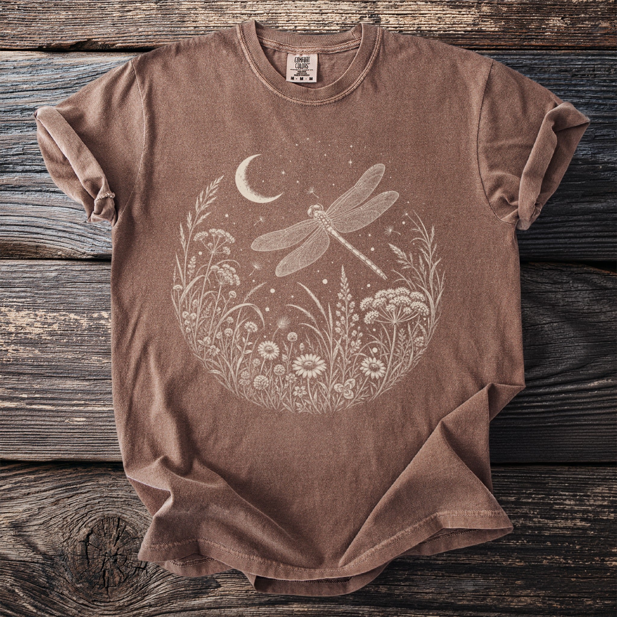 Brown t-shirt with a white circular design of a dragonfly, moon, and wildflowers.