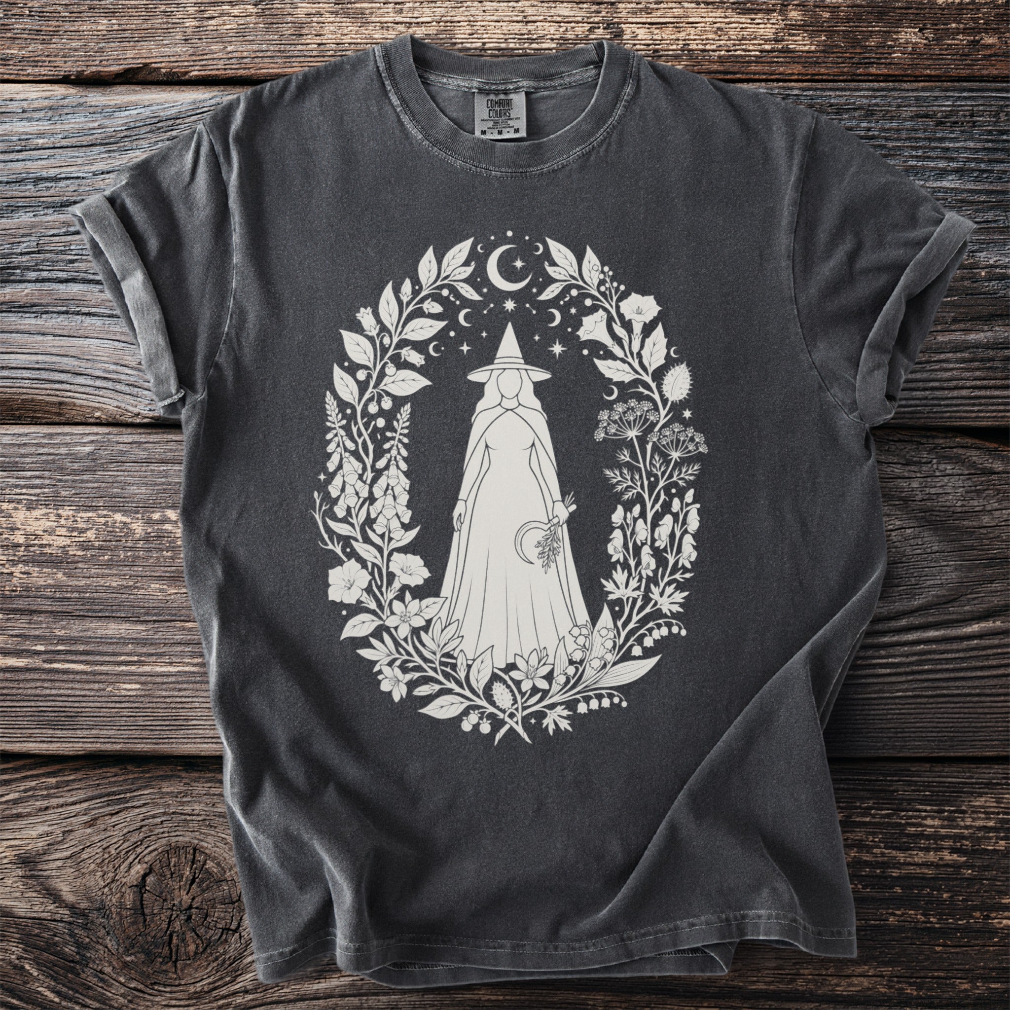 Dark gray t-shirt with white oval design of a witch illustration in floral wreath.