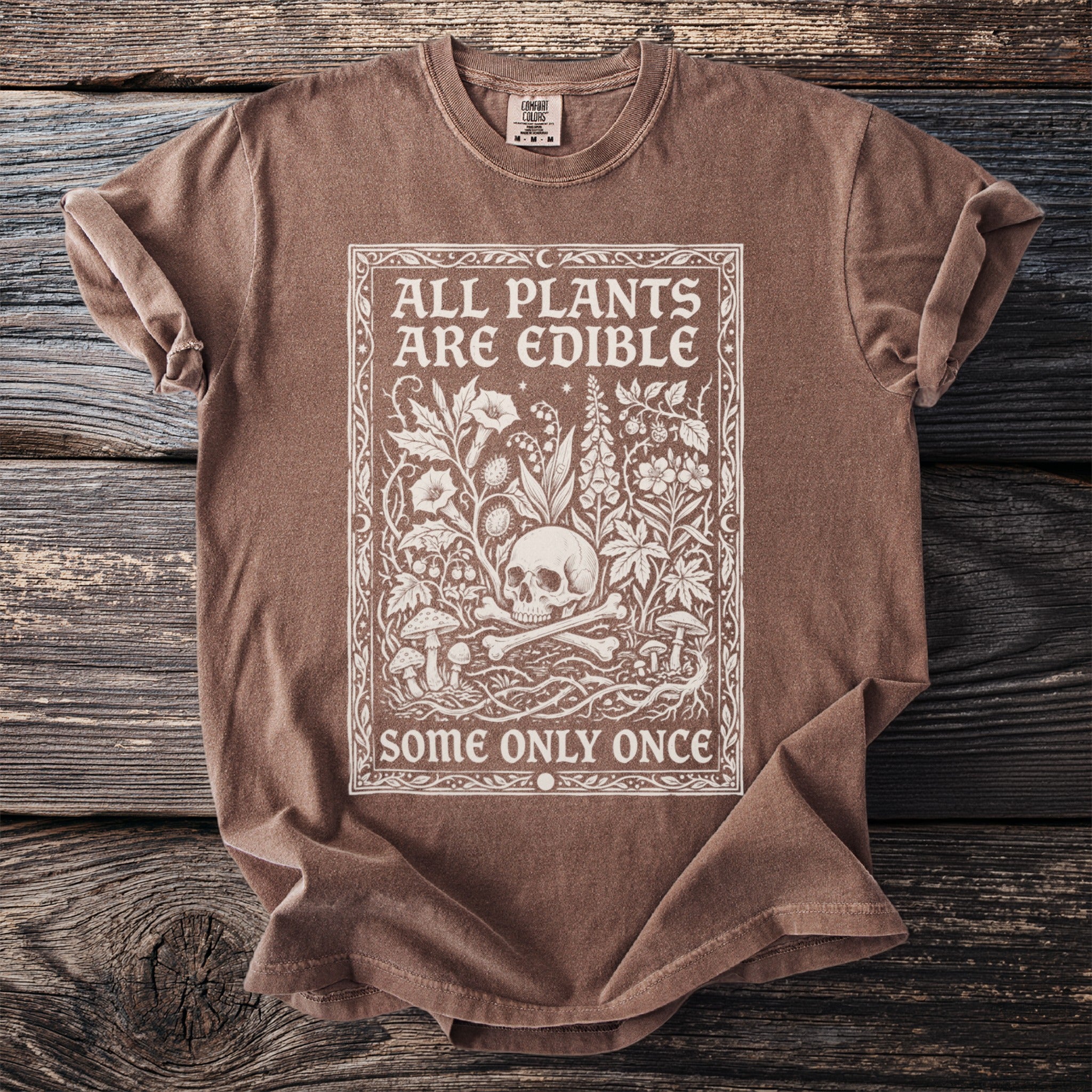 Brown t-shirt with white graphic of a skull, bones, plants, and text.