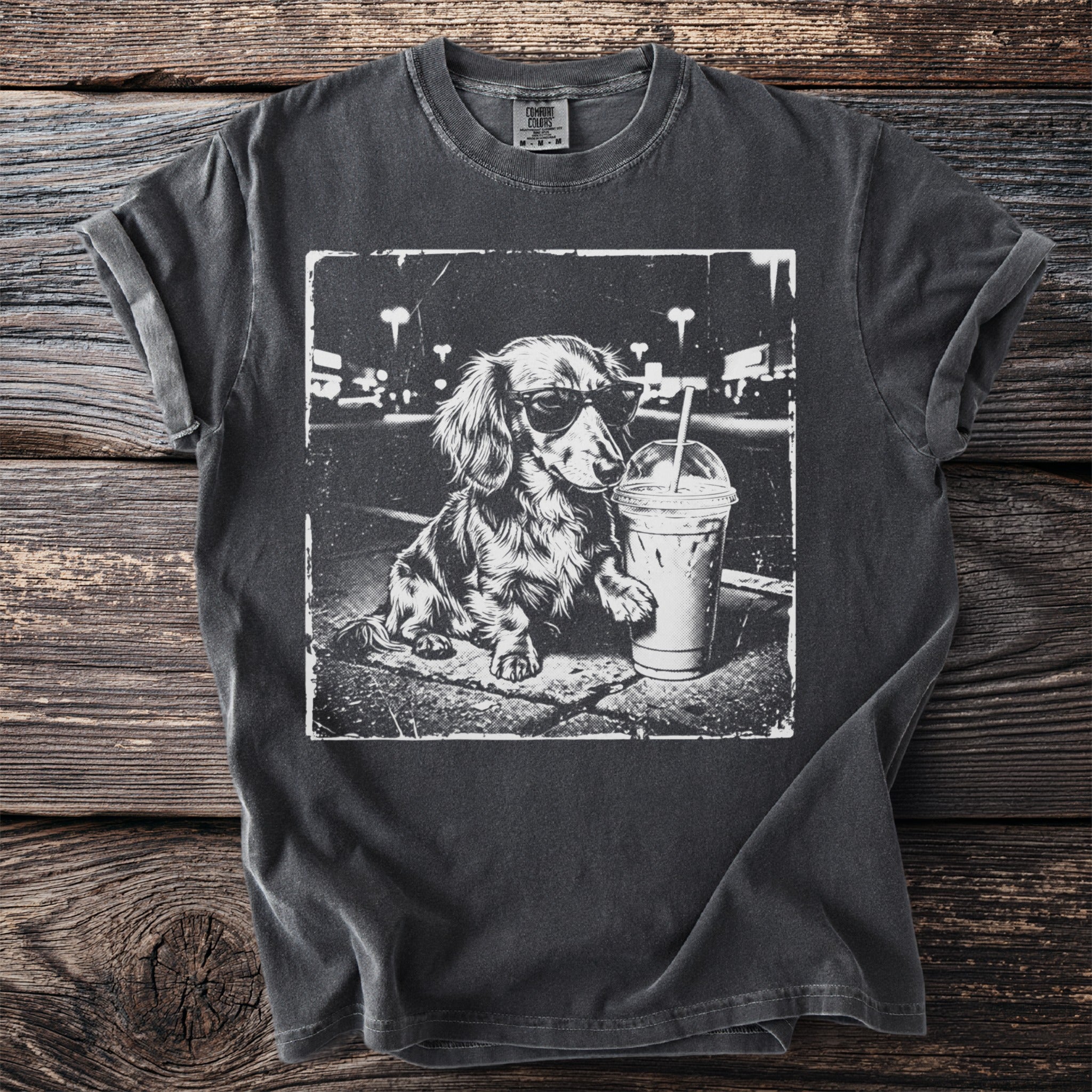 Dachshund wearing sunglasses with iced coffee on a dark t-shirt.