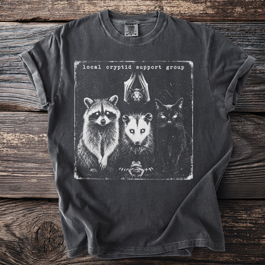 Dark t-shirt with graphic of raccoon, opossum, bat, cat, and frog and text "local cryptid support group".
