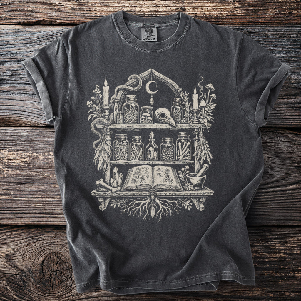 Dark t-shirt with a witchy altar graphic featuring jars, candles, and an open book.