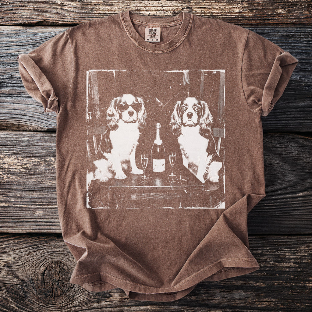 Brown t-shirt with a white graphic of two dogs, champagne, and glasses.