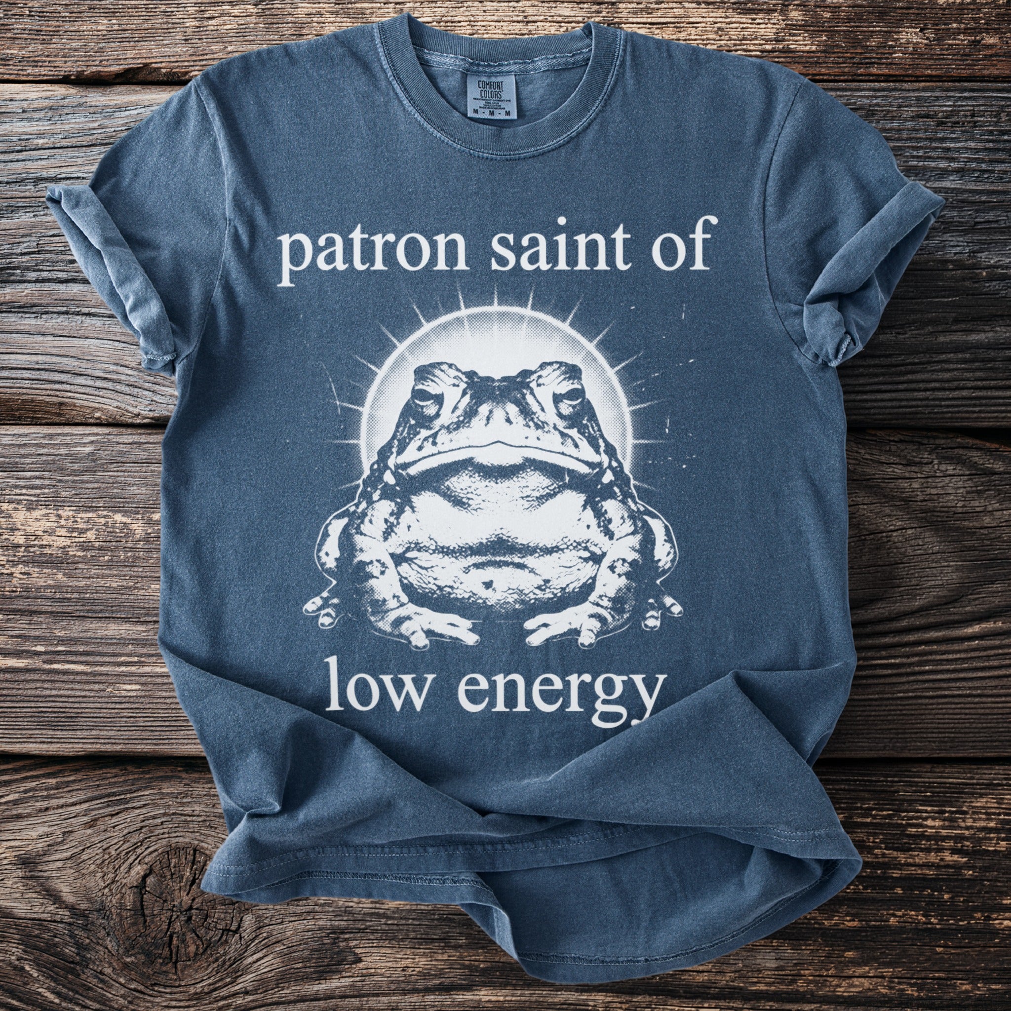 Blue t-shirt graphic with a toad and text "patron saint of low energy".