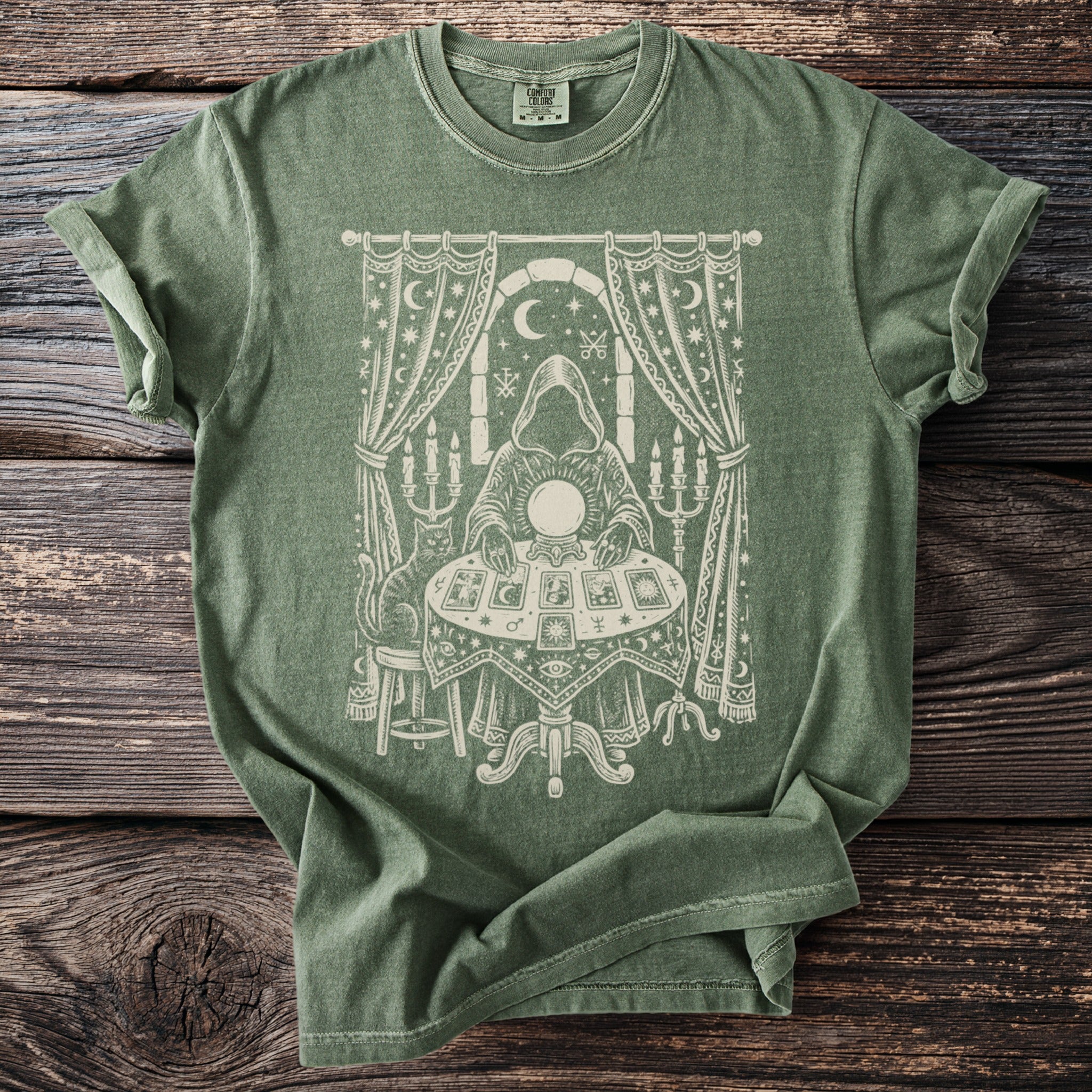 Green t-shirt with a cream screen-print of a fortune teller with a crystal ball, tarot cards, and a cat.