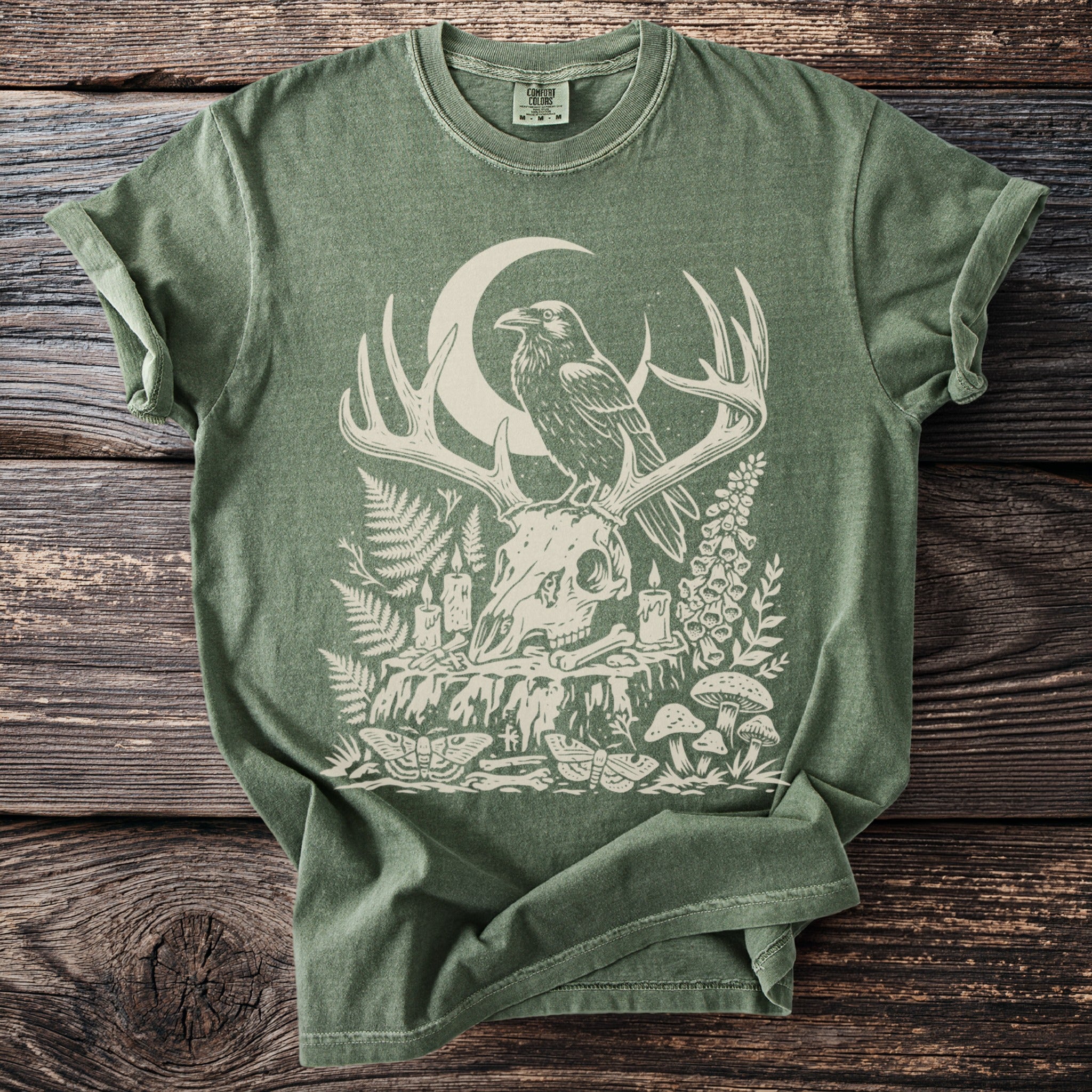 Green t-shirt with skull, raven, crescent moon, mushrooms, and candles graphic.