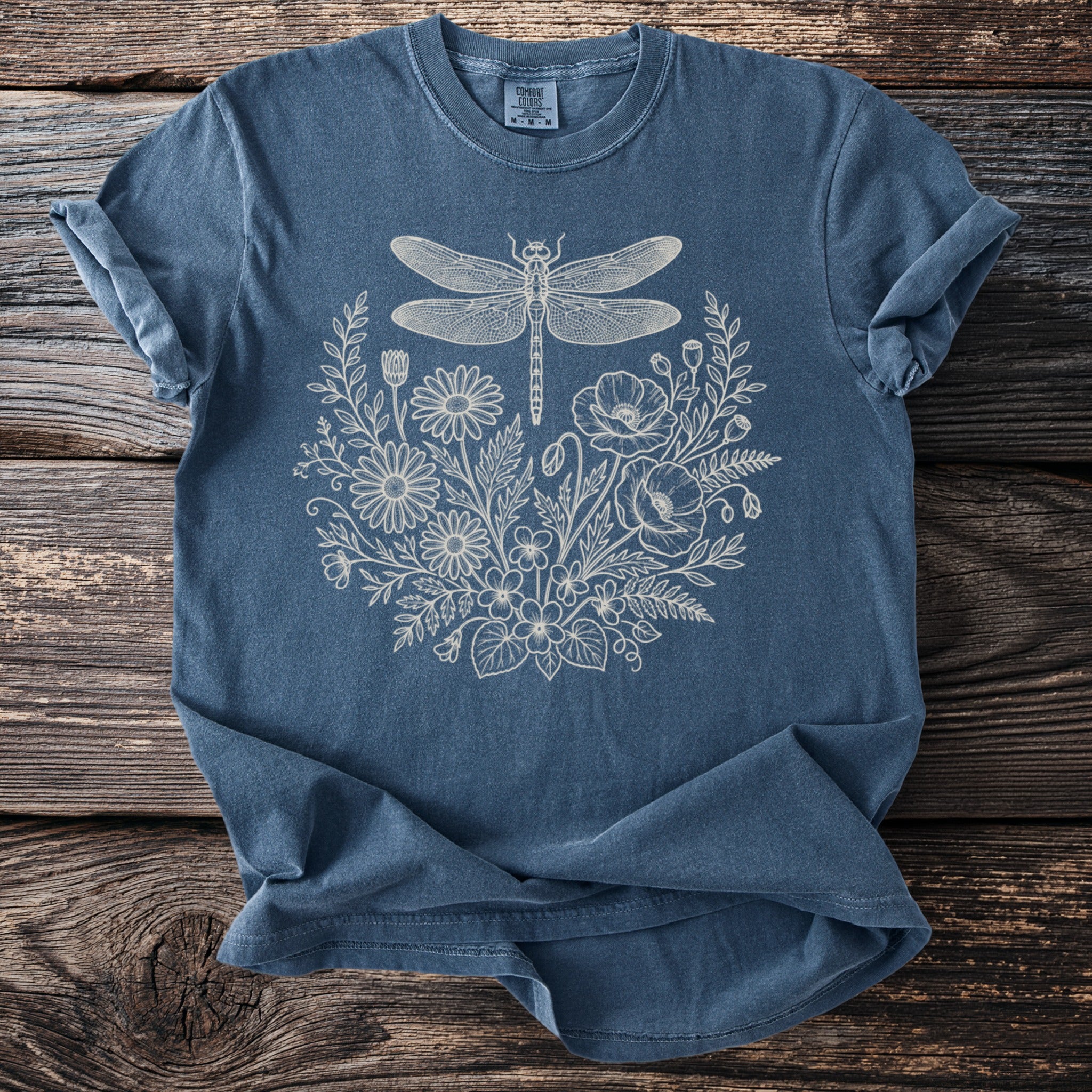 Blue t-shirt with a cream outline of a dragonfly and floral wreath design.