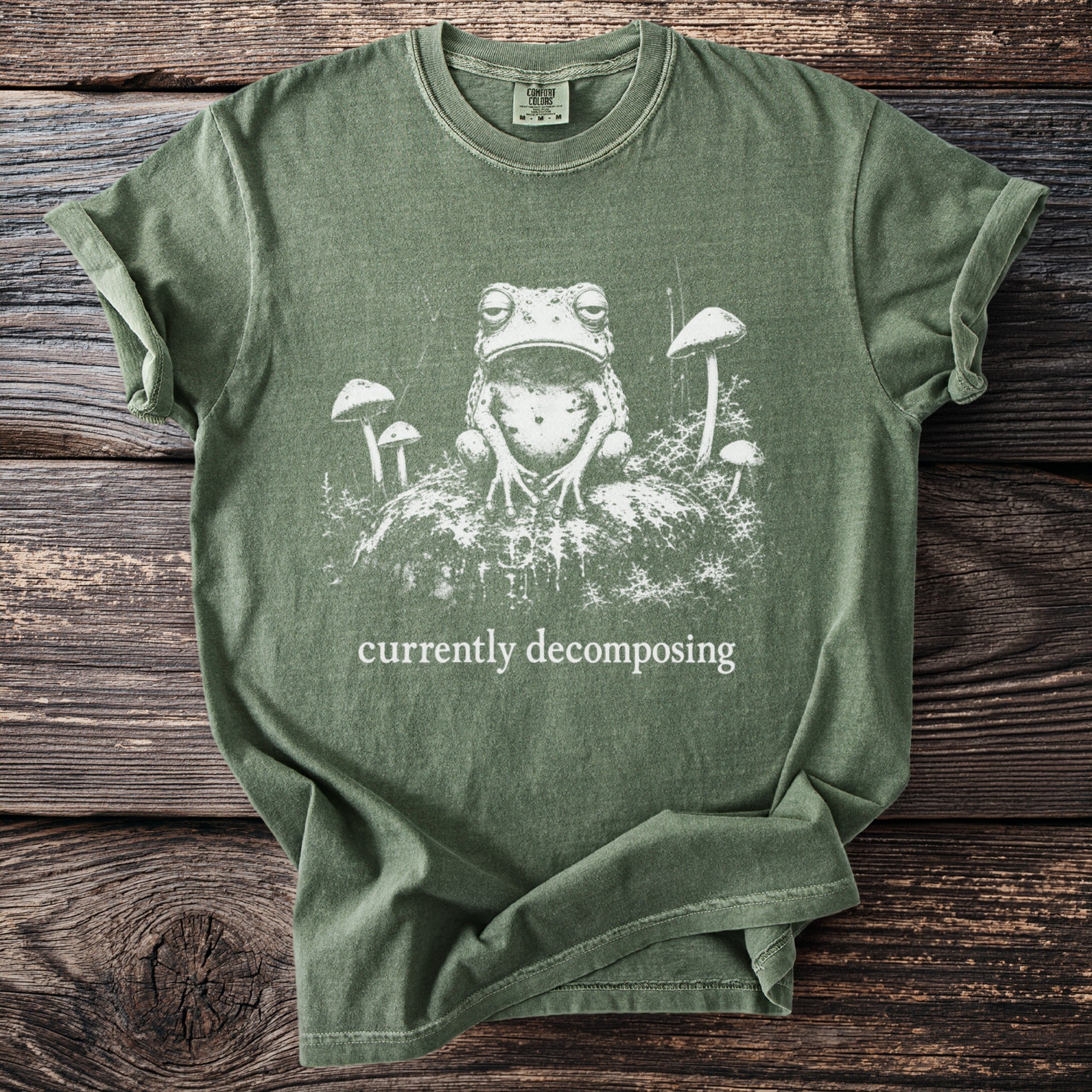 Green t-shirt with a distressed print of a frog and mushrooms, reads "currently decomposing".