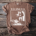 Brown t-shirt with "it is what it is" text and a werewolf character holding coffee.