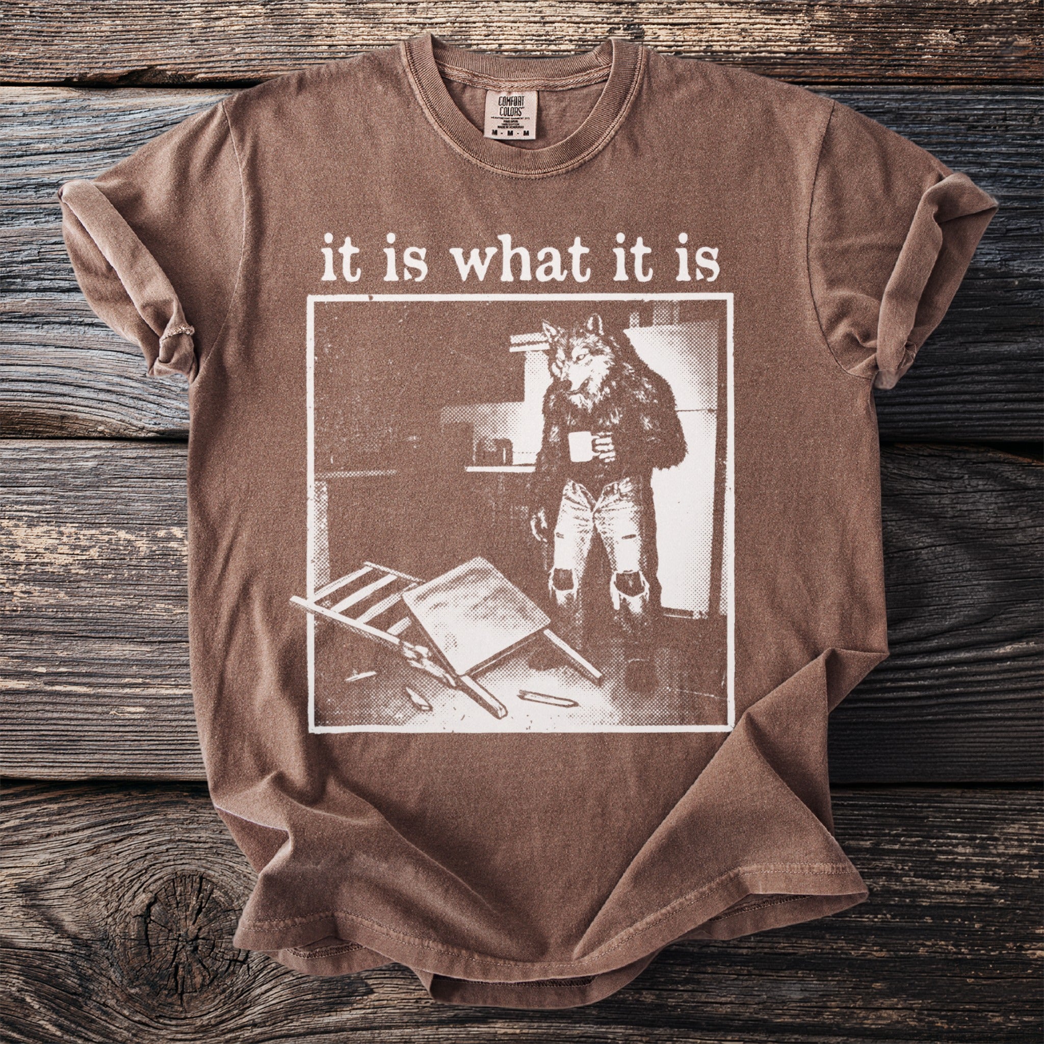 Brown t-shirt with "it is what it is" text and a werewolf character holding coffee.