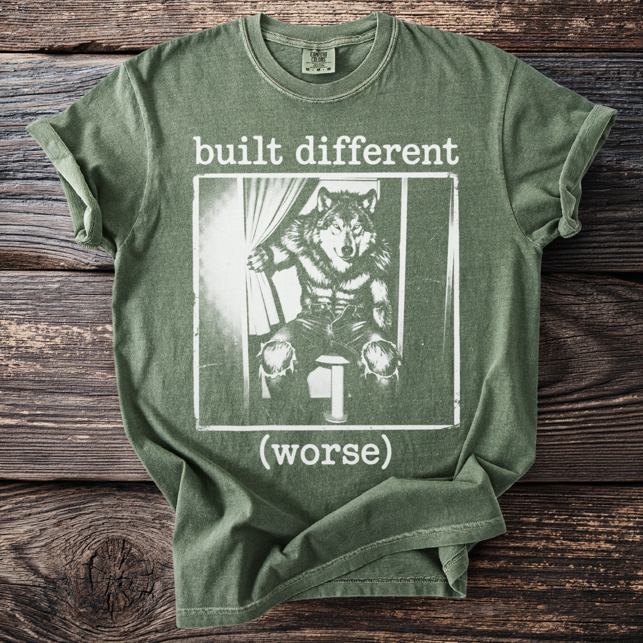 Green t-shirt with a graphic of a wolf in clothes and text "built different (worse)".