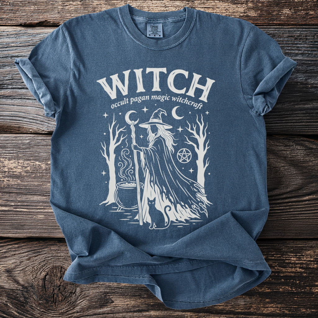 Blue t-shirt with white graphic of a witch, cauldron, cat, trees, and text: WITCH occult pagan magic witchcraft
