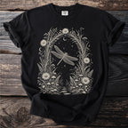Black t-shirt with a cream-colored botanical illustration of a dragonfly surrounded by flowers and stars.