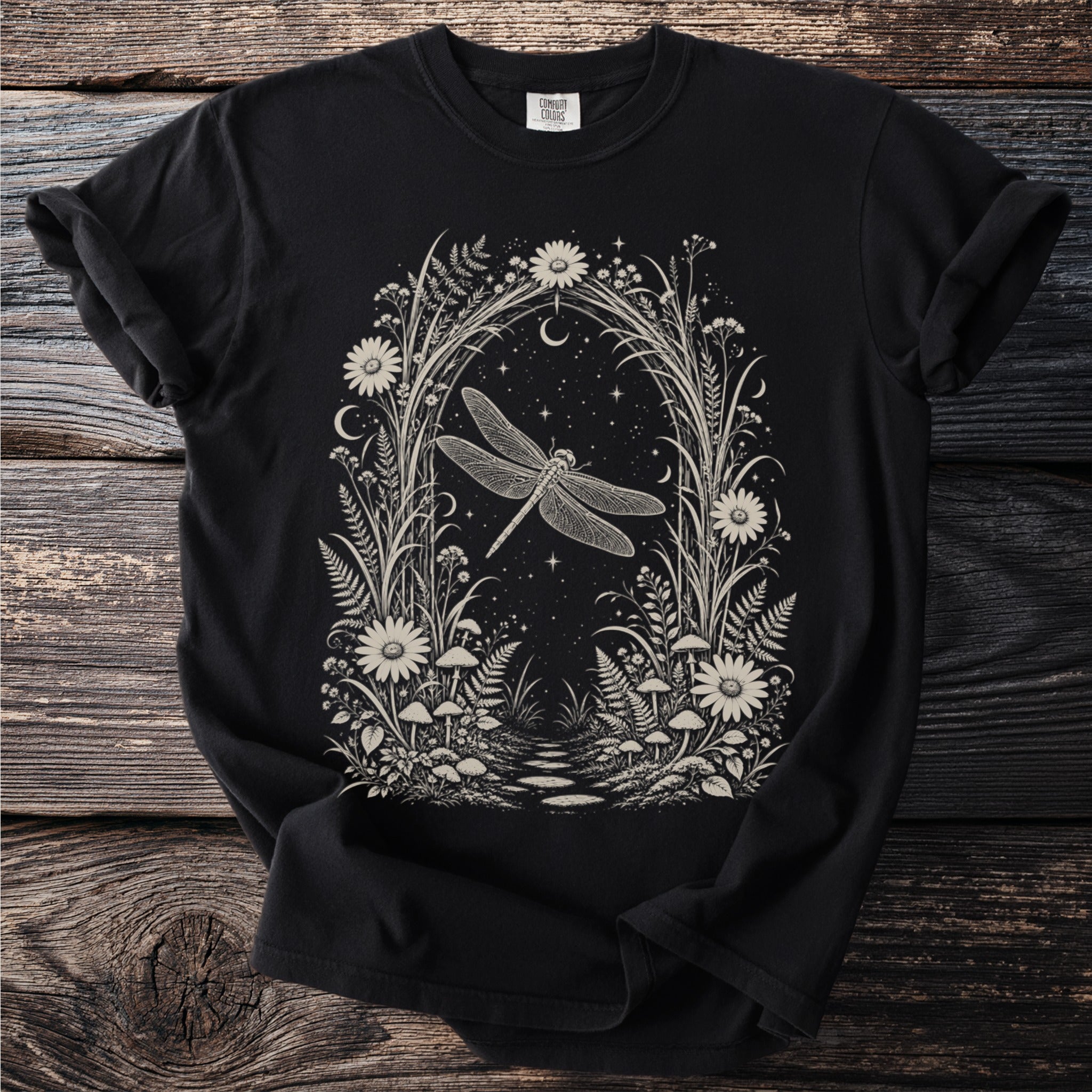 Black t-shirt with a cream-colored botanical illustration of a dragonfly surrounded by flowers and stars.