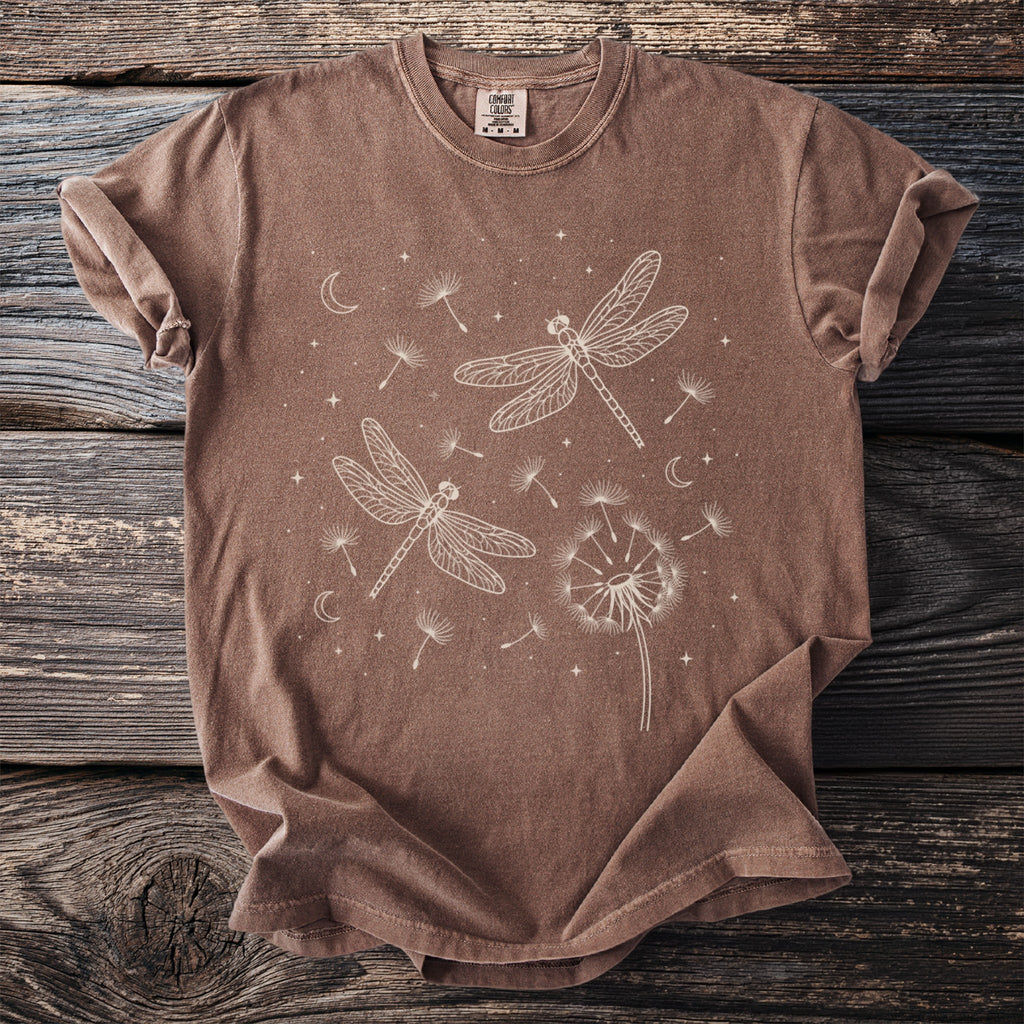 Brown t-shirt with white line art of dragonflies, dandelions, moons, and stars.