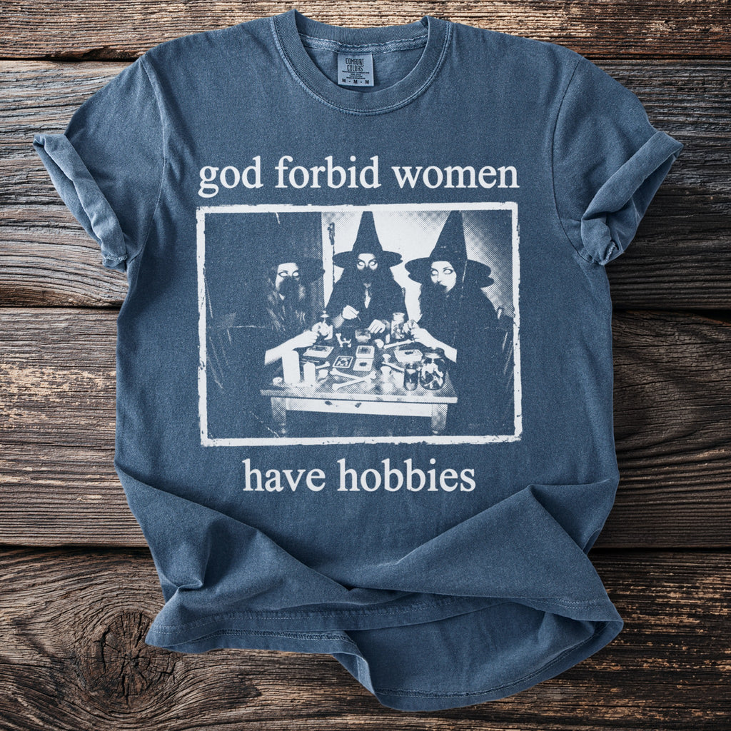 Blue t-shirt with "god forbid women have hobbies" text and image of three witches.