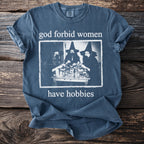 Blue t-shirt with "god forbid women have hobbies" text and image of three witches.