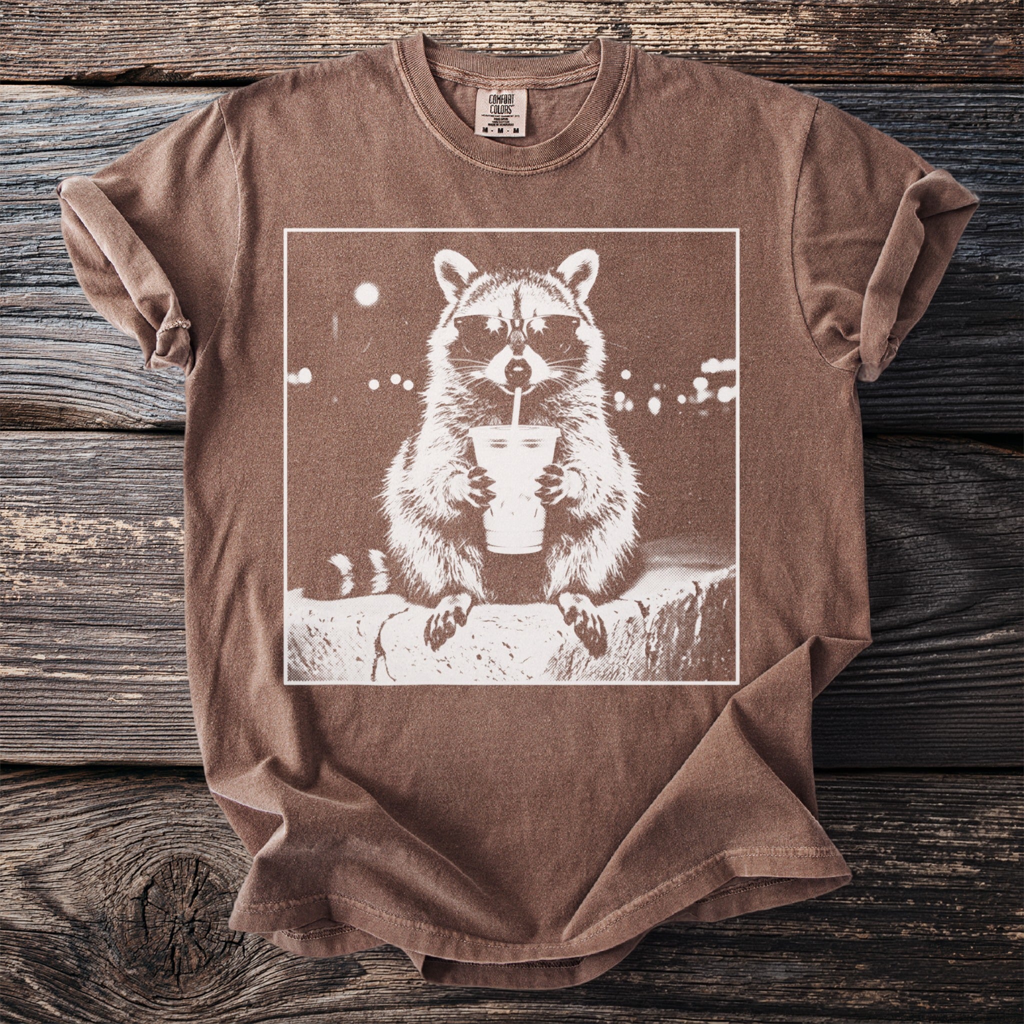 T-shirt with a white graphic of a raccoon wearing sunglasses drinking from a cup.