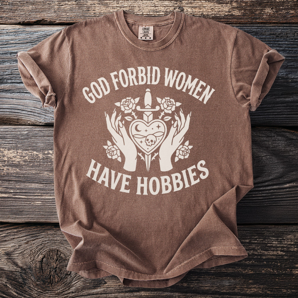 Brown t-shirt with white text and graphic that reads "God forbid women have hobbies".