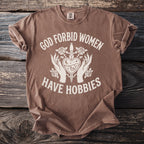 Brown t-shirt with white text and graphic that reads "God forbid women have hobbies".