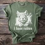 Olive green t-shirt with a white graphic of a squirrel and text reading "i have rabies".