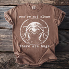 Brown t-shirt with white text "you're not alone" and a round graphic of a smiling beetle, followed by "there are bugs".