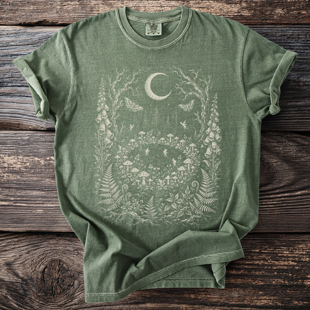 Green t-shirt with moon, fairies, and woodland creatures illustration on distressed wood background.