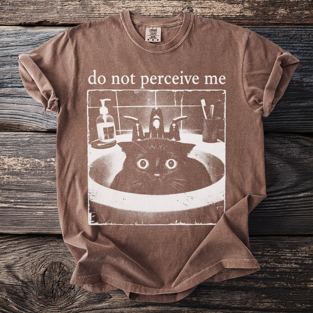 Brown t-shirt with "do not perceive me" text and a cat in a sink graphic.