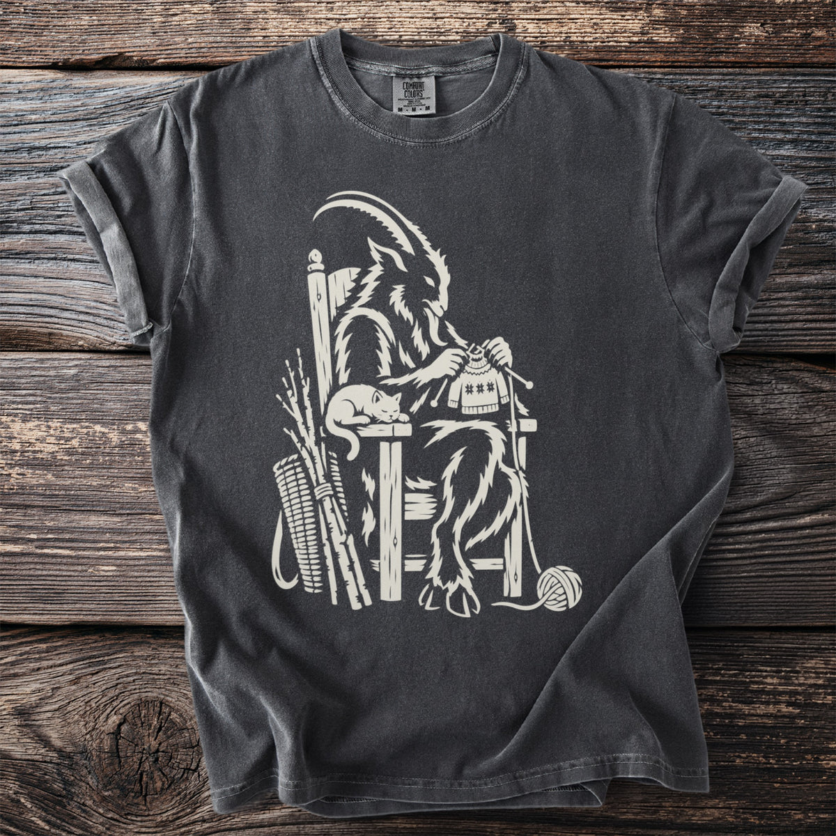 A goat-like figure sits knitting with a cat on its lap and a basket of twigs.