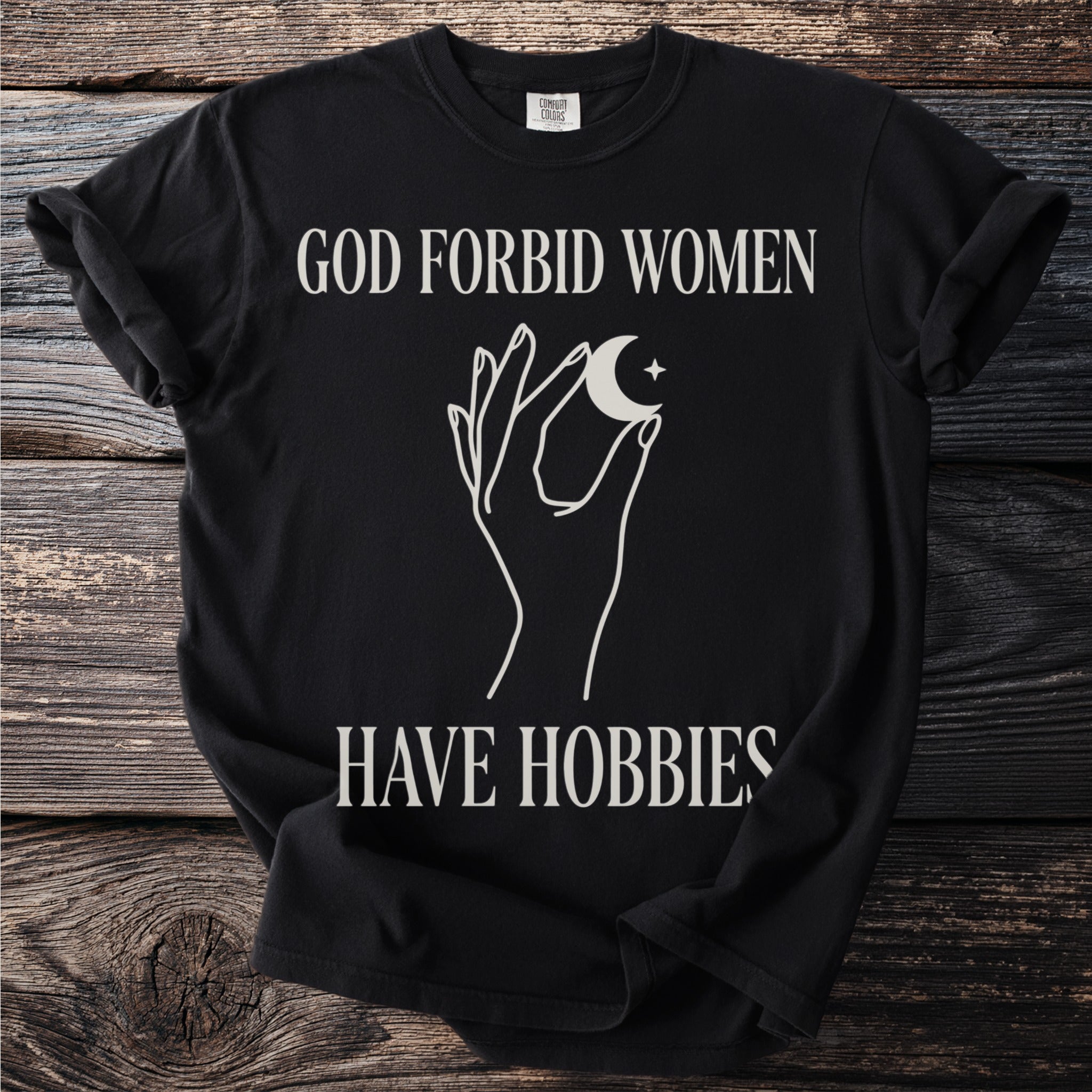 Black t-shirt with text "GOD FORBID WOMEN HAVE HOBBIES" and celestial graphic.