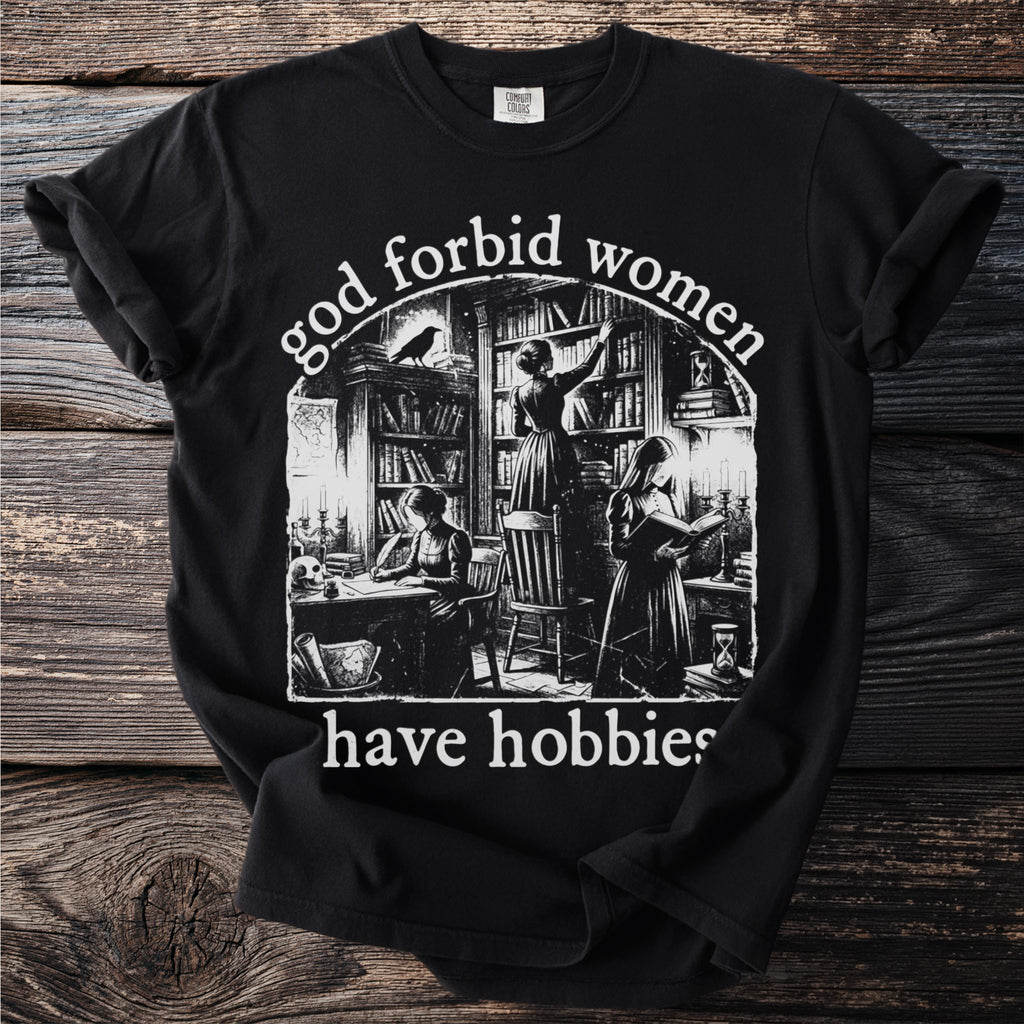Black t-shirt with "god forbid women have hobbies" text and library illustration.