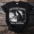 Black t-shirt with "god forbid women have hobbies" and a silhouette of someone at a desk.