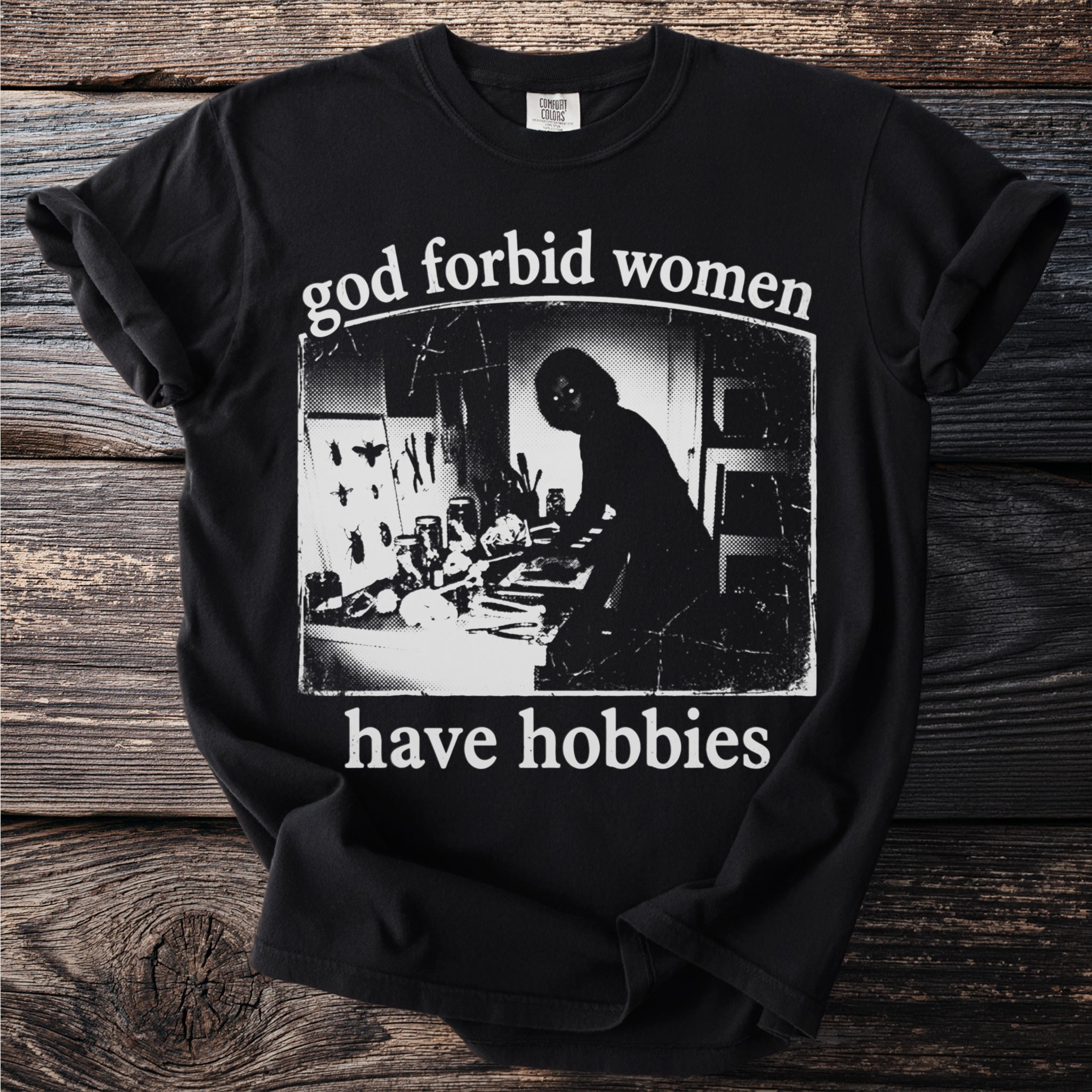 Black t-shirt with "god forbid women have hobbies" and a silhouette of someone at a desk.