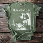 Green t-shirt with "it is what it is" text and a wolf in jeans holding coffee.