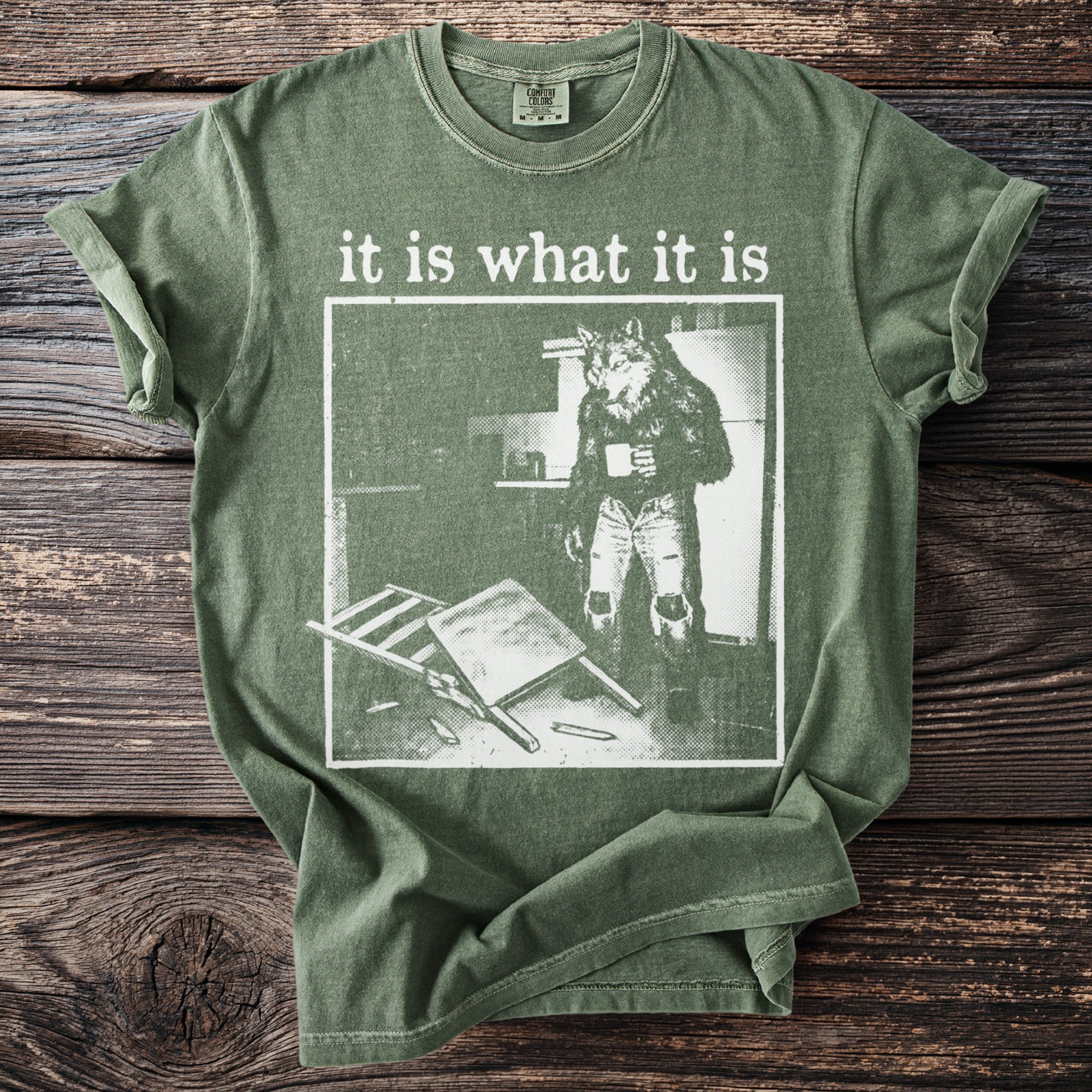 Green t-shirt with "it is what it is" text and a wolf in jeans holding coffee.